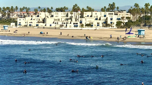 Um hotel à beira-mar com vários edifícios, praia e surfistas na água.