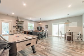 A spacious living area with a pool table, a dining area with a table and chairs, and a kitchen with a refrigerator and shelves.
