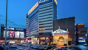 Un hotel de varios pisos con un letrero llamativo, un estacionamiento con coches y edificios comerciales aledaños.