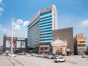 A multi-story hotel with a prominent sign, a parking lot with several cars, and a clear sky.