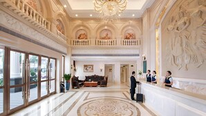 Un vestíbulo amplio con candelabro, pisos de mármol y una recepción.
