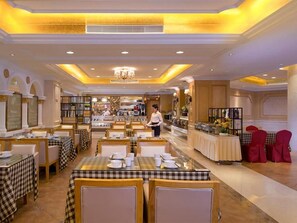 Un salón de comidas de hotel con manteles a cuadros, un bufé y un camarero.