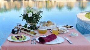 Tavola imbandita con cibo e bevande a bordo piscina, con frutta, pane e salse.
