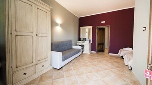 Una stanza con un armadio grande, un divano grigio, un piccolo tavolo con uno specchio e un letto con copripiumino bianco.