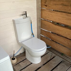 Eine weiße Toilette mit Tank und einem blauen Schlauch, platziert auf einer Holzplattform.