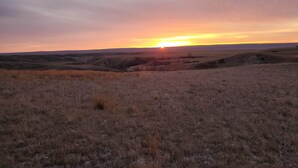 Weite Landschaft mit sanften Hügeln und einem Sonnenuntergang in der Ferne.