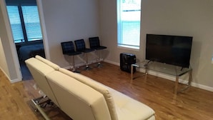 A living room with a reclining sofa, a glass coffee table, a flat-screen TV, and a window with blinds. - ⁎ 2 Townhomes with Smart TV & Blackout Curtains (Renton)