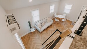 A spacious loft apartment with a herringbone wood floor, a white sofa, a small round table with chairs, and a staircase leading to an upper level. - The Loft w/outdoor fire pit (Grandville)