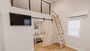 A loft bedroom with a bed, a TV, a ladder, and a window. - The Loft w/outdoor fire pit (Grandville)