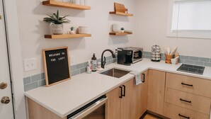 A modern kitchen with wooden cabinets, a built-in dishwasher, a coffee maker, and a chalkboard sign. - The Loft w/outdoor fire pit (Grandville)