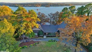 Une maison avec un toit en pente, entourée d’arbres aux feuilles d’automne, et offrant une vue sur un lac.