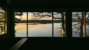 Une pièce dotée d’une grande fenêtre donnant sur un lac paisible et des arbres, avec un banc au premier plan.