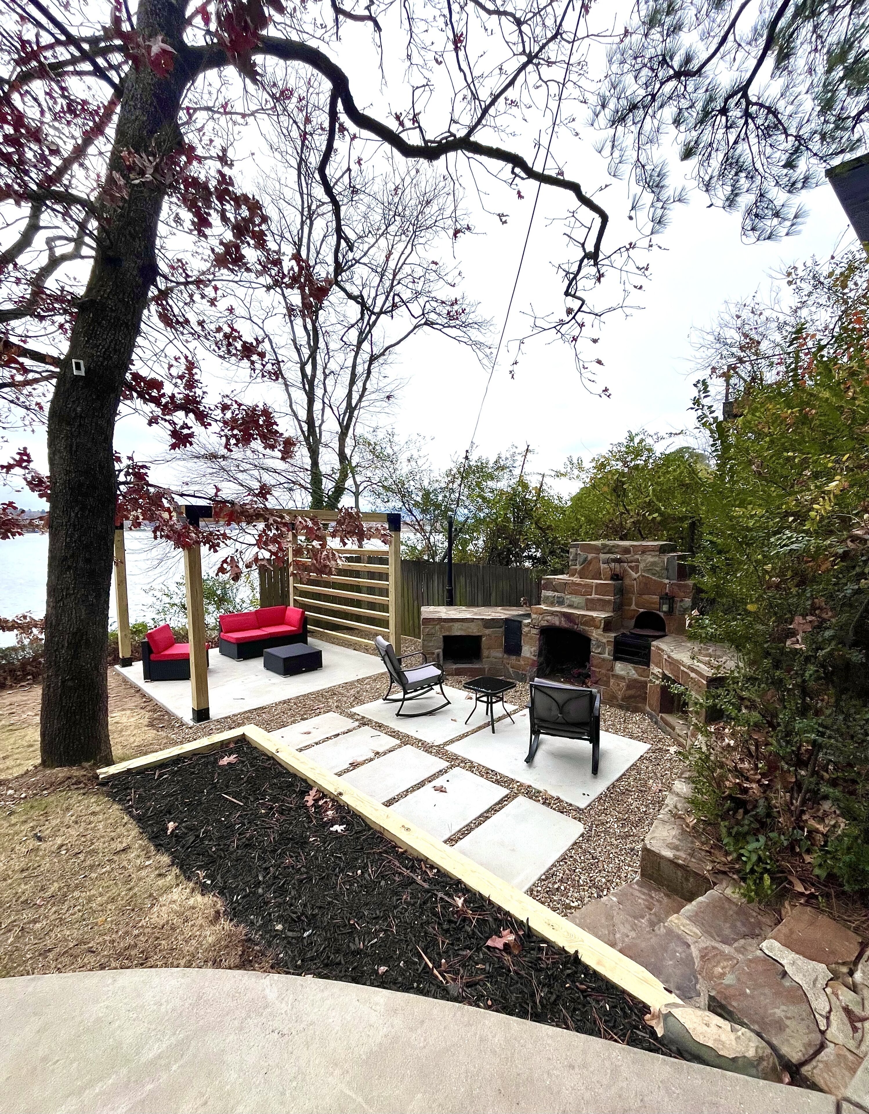Un espace extérieur aménagé en terrasse, avec une cheminée en pierre, des sièges et une vue sur l’eau.