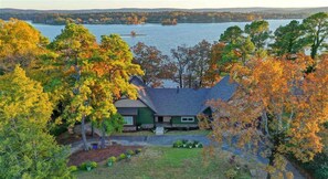 A house with a sloped roof, surrounded by trees with autumn foliage, and a view of a lake.