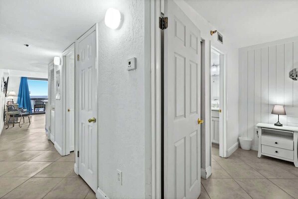 A hallway with white doors, a view of the sky through a window, and a small table with a lamp. - SunDestin 1BR Beach Retreat With Relaxing Gulf-Front Balcony - Unit 0306 (Destin)