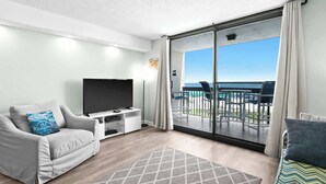 Een moderne hotelkamer met een balkon, een flatscreen televisie, een bank en een salontafel.