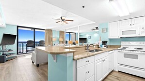 A modern kitchen with a large island, white cabinets, and a view of the ocean. - SunDestin 1BR Condo With Tropical Style and Gulf Sunsets - Unit 0408 (Destin)