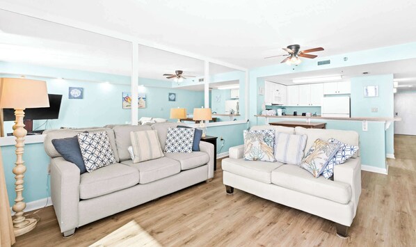 A modern living room with two sofas, a coffee table, and a TV. The room has a wooden floor and light blue walls. - SunDestin 1BR Condo With Tropical Style and Gulf Sunsets - Unit 0408 (Destin)