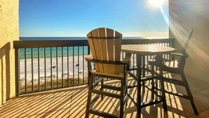 A balcony with a wooden chair and table, overlooking a beach with a clear sky and sun shining. - SunDestin Resort Unit 0706 (Destin)
