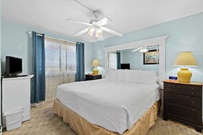 Un dormitorio con una cama, ventilador de techo, televisor, cómoda y mesita de noche con lámparas.