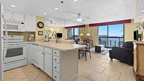 A modern kitchen with white cabinets, a central island, and a dining area with a view. - Beachfront 1BR Condo With Balcony, King Bed and Coastal Style (Destin)
