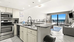 Una cucina moderna con isola centrale, elettrodomestici in acciaio inossidabile e vista sull'oceano dal balcone.