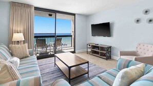 A modern hotel room with a large balcony, a sofa set, a coffee table, a TV, and a small TV stand.