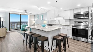 A modern kitchen with a central island, bar stools, stainless steel appliances, and a view to the outside.