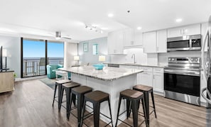 Una cocina moderna con una isla central, taburetes de bar, electrodomésticos de acero inoxidable y vistas al exterior.
