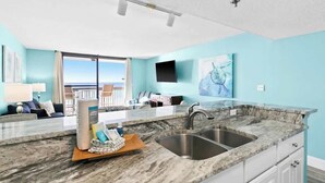 A modern kitchen with a marble countertop, a double sink, and a view of the balcony.