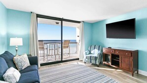 A living room with a sofa, a TV, a wooden cabinet, and a view of the balcony.