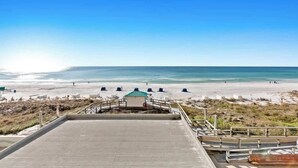 Vista sulla spiaggia con una passeggiata in cemento che conduce a un gazebo, sedie a sdraio e ombrelloni.