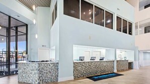 Una hall moderna di un hotel con una reception, un balcone al secondo piano e vista sul parcheggio.