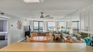 A spacious living room with a large dining table, comfortable seating, a ceiling fan, and a view of the ocean.