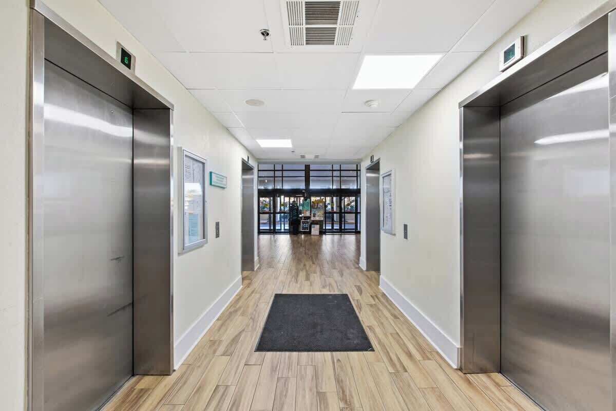A modern elevator lobby with a wooden floor and a black mat at the entrance.
