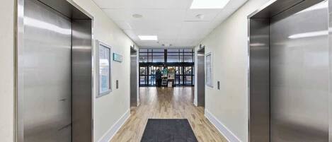 A modern elevator lobby with a wooden floor and a black mat at the entrance.