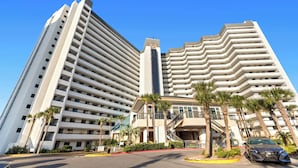 Een hotel met meerdere verdiepingen, met een modern design, balkons, een centraal torentje en palmbomen op de voorgrond.