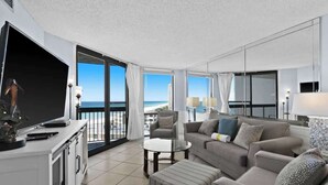 Una sala de estar moderna con un televisor de pantalla plana grande, un sofá, una mesa de centro y un balcón con vista a la playa.