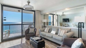 A living room with a large sliding glass door leading to a balcony with a view of the ocean. There is a sofa, a chair, and a coffee table. - Relaxing 1BR Gulf-front condo with balcony and coastal views (Destin)