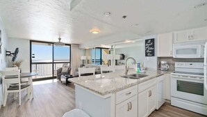 A modern kitchen with a large island, white cabinetry, and a view to the outside. - Relaxing 1BR Gulf-front condo with balcony and coastal views (Destin)