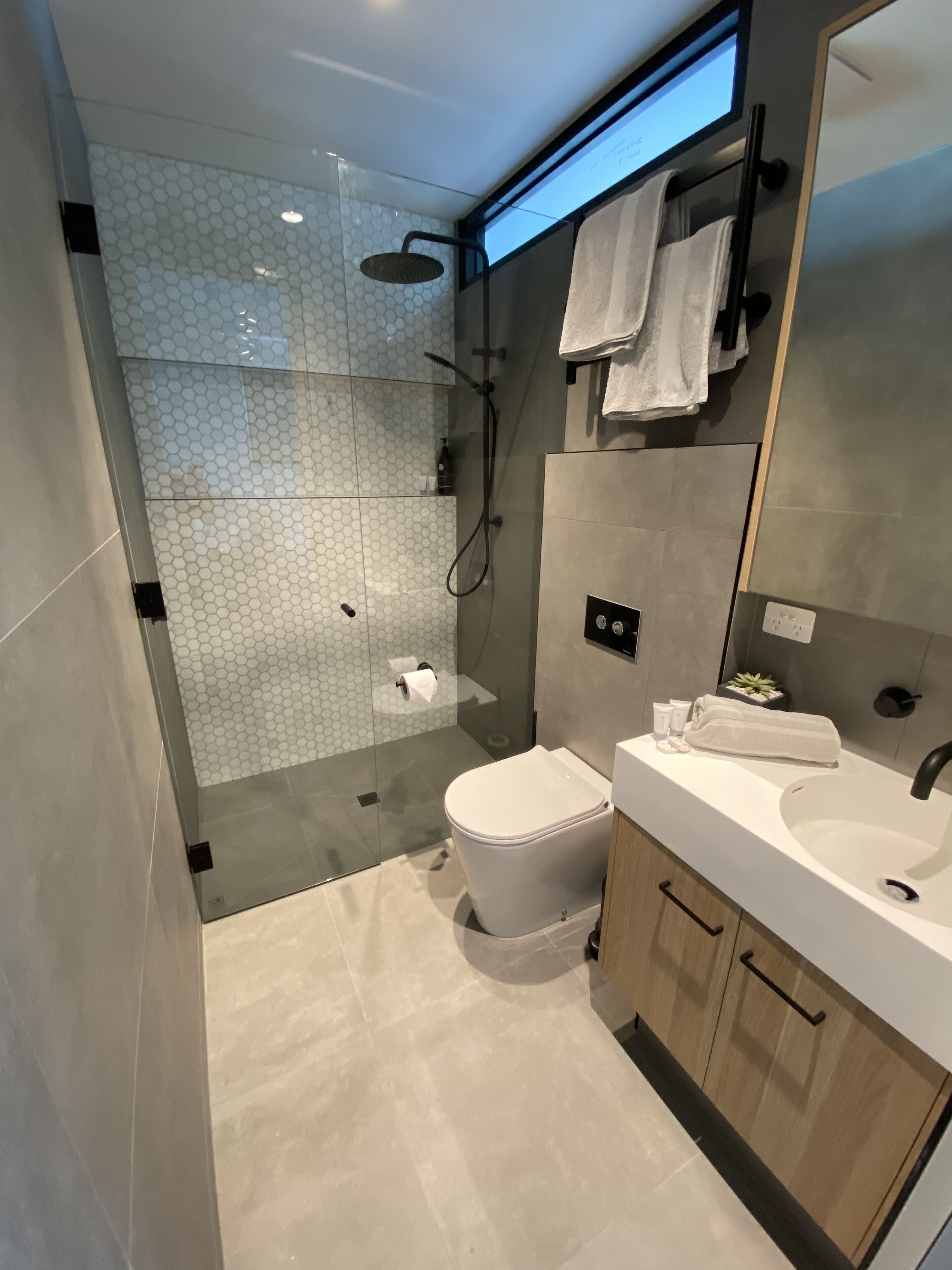 A modern bathroom with a glass-enclosed shower, a toilet, and a vanity with a sink and mirror.