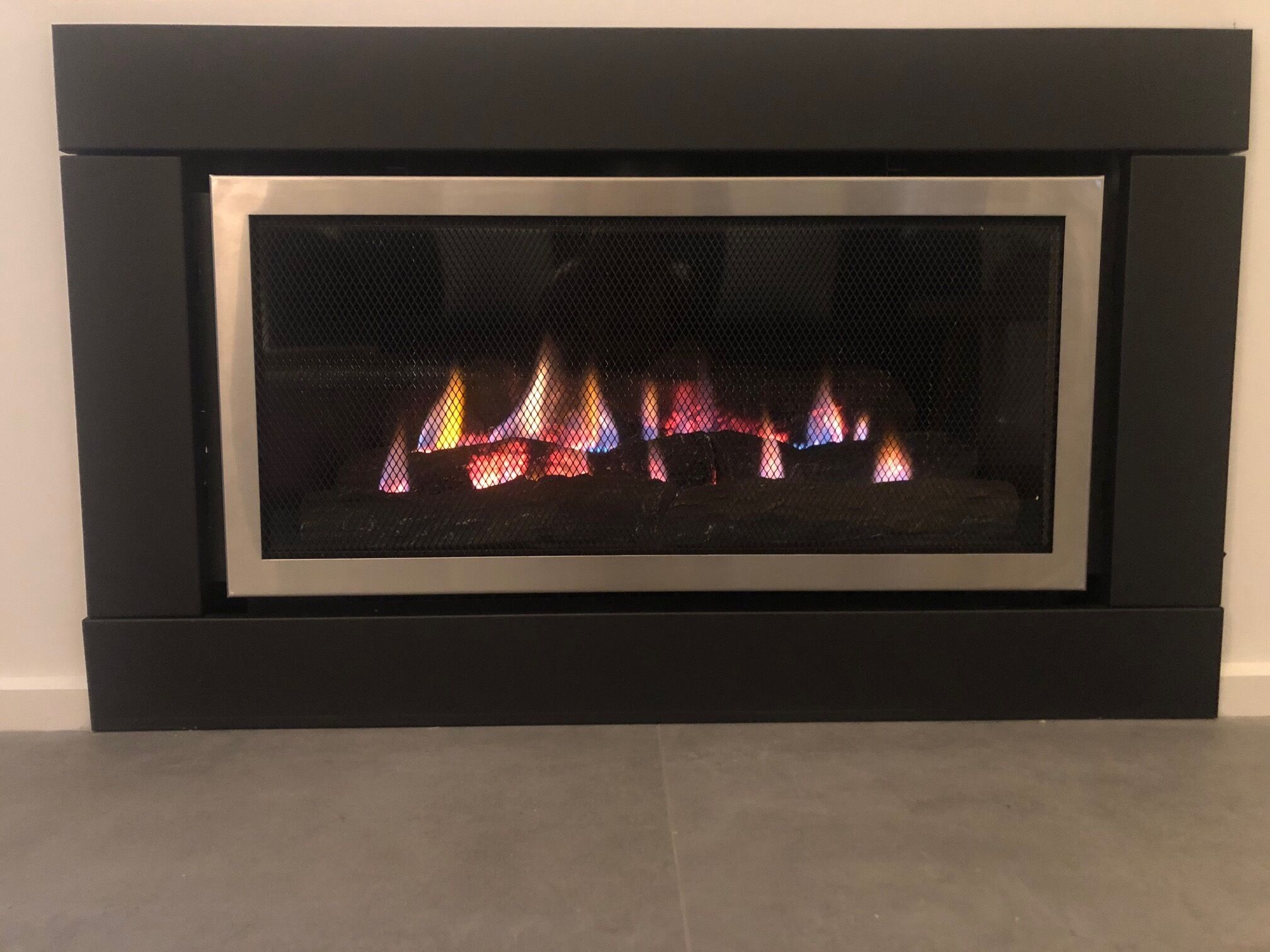 A modern fireplace with a glass front, displaying a colorful fire.