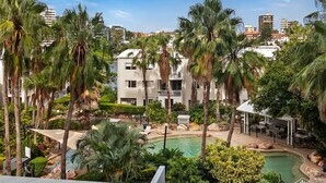Een resort met een zwembad, palmbomen en moderne gebouwen op de achtergrond.