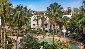 Een resort met een zwembad, palmbomen en moderne gebouwen op de achtergrond.