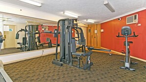 Een sportschool met fitnessapparatuur, een grote spiegel en een rode wand.