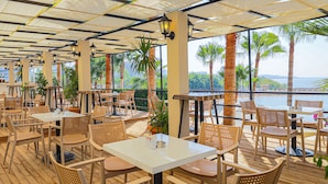 An outdoor dining area with tables and chairs, surrounded by palm trees and a view of the sea. - Crystal Land Of Paradise Beach Hotel (Alanya)