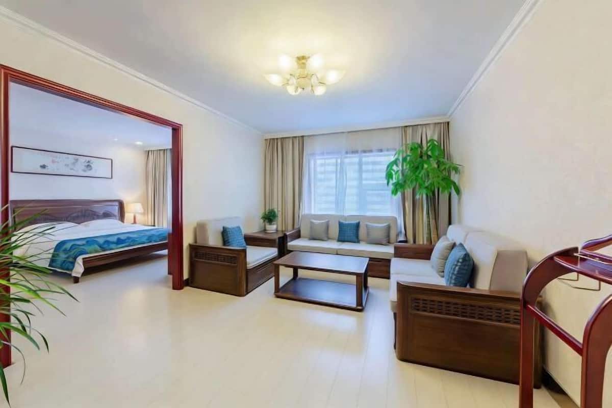 Una habitación de hotel con cama, sofá, mesa de centro y un ventanal con cortinas.