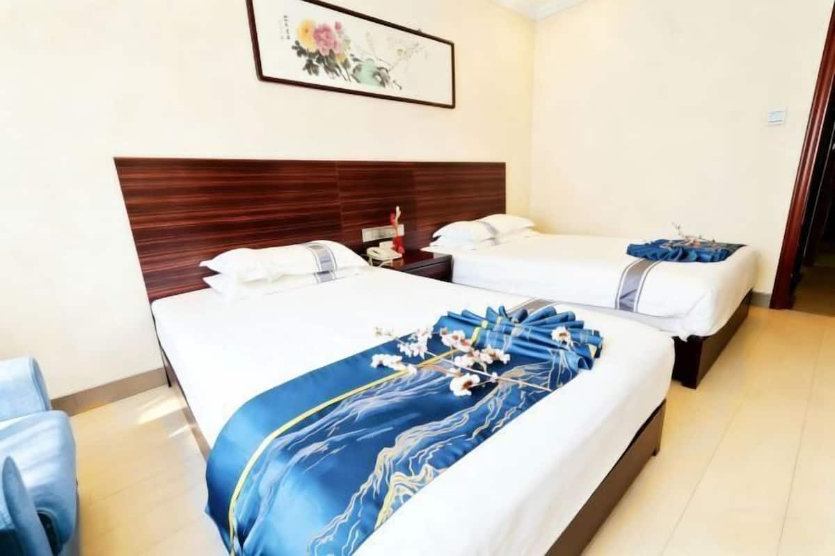 Habitación de hotel con dos camas, cabecera de madera, un cuadro en la pared y colcha de flores azules.