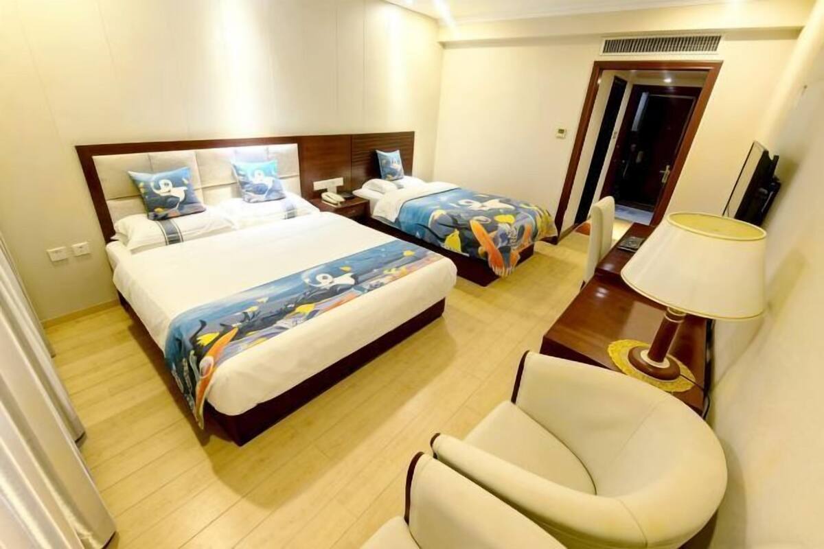 Habitación de hotel con dos camas, una silla, una mesita de noche y una lámpara.