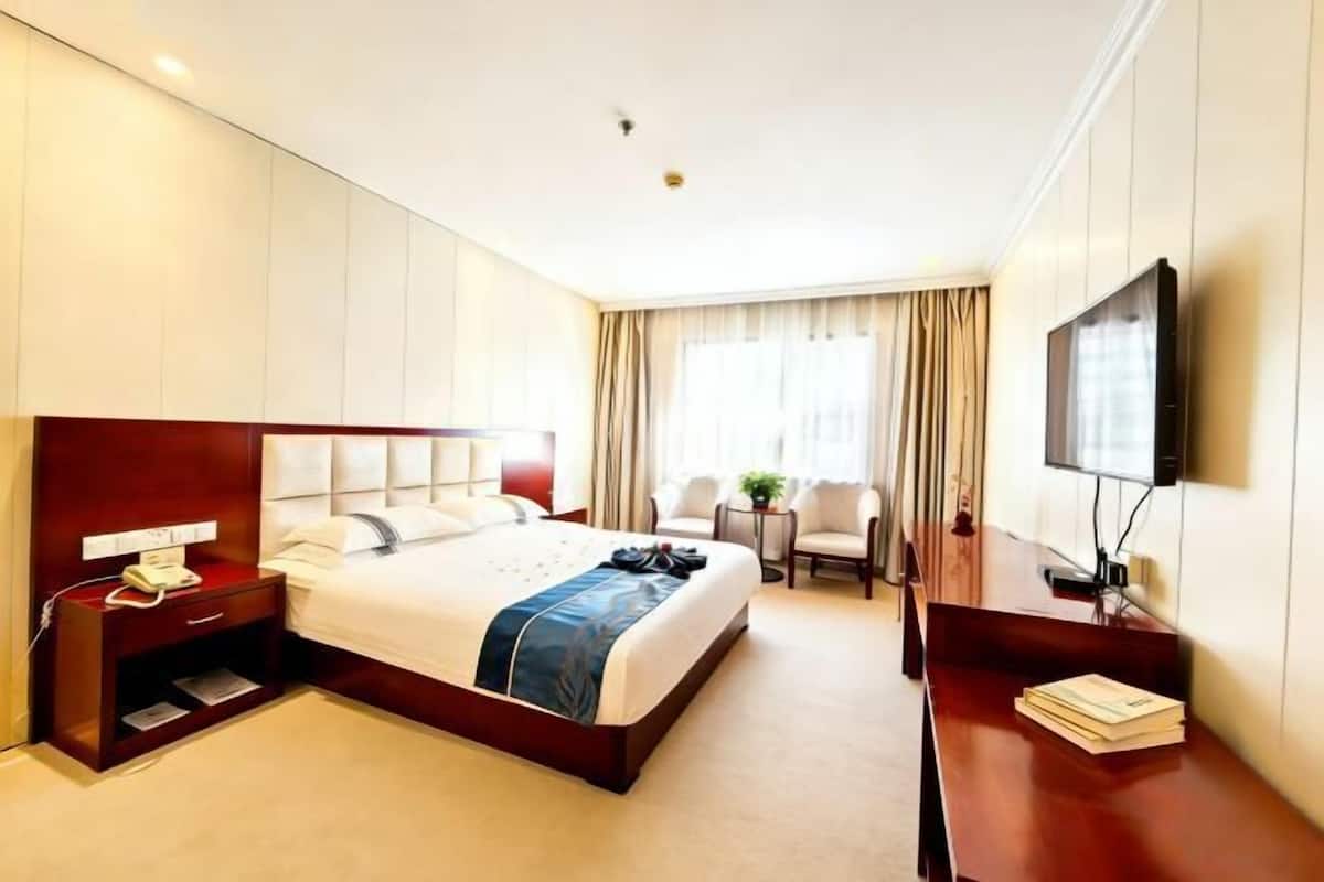 Una habitación de hotel con cama, mesita de noche, televisión, escritorio y sillas.